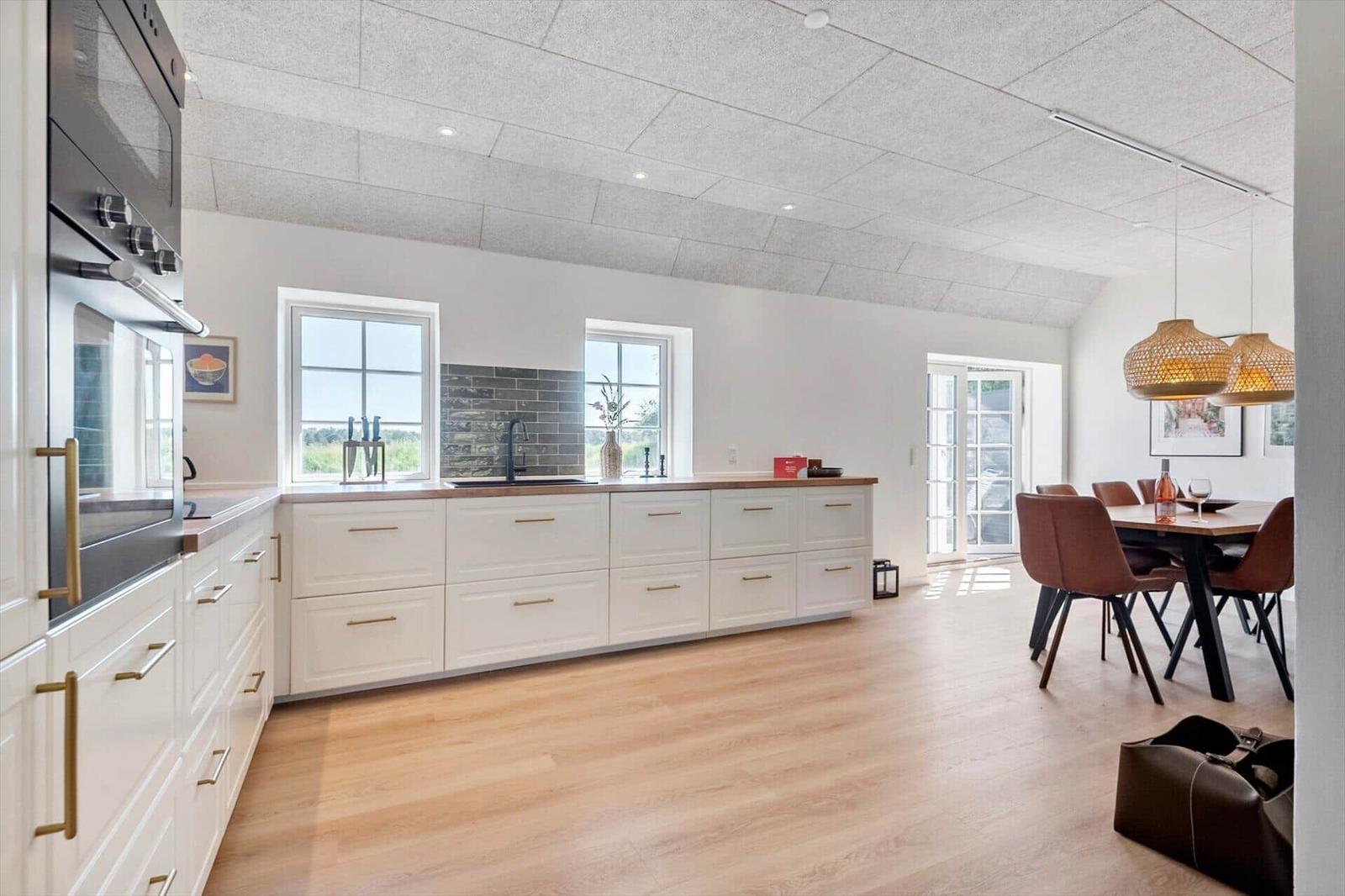 Küche mit Essbereich, weiße Schränke, Holzboden und Fenster zur Außenseite.