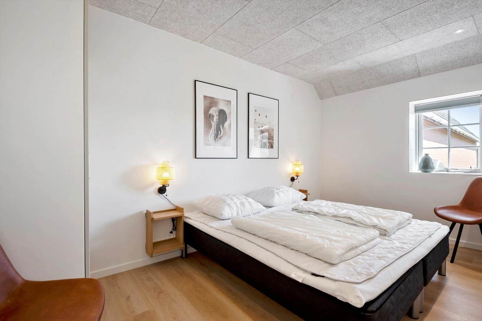 Schlafzimmer mit Doppelbett, zwei Wandlampen und zwei Bildern an der Wand.