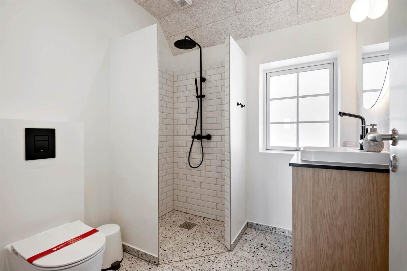Badezimmer mit Dusche, Waschbecken und Toilette. Weiße Fliesen und Holzoptik.