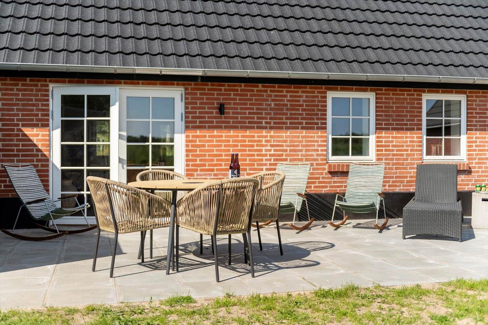 Terrasse mit Tisch, Stühlen und Liegen vor einem Backsteinhaus mit Dach.