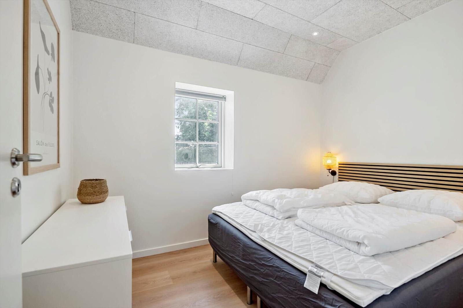 Schlafzimmer mit Doppelbett, Fenster und Wandlampe.