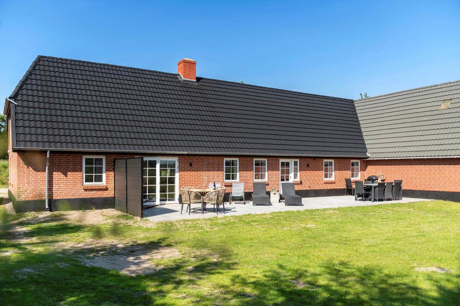 Rotes Backsteingebäude mit Terrasse und Garten. Außentisch, Sitzgelegenheiten und Grill.
