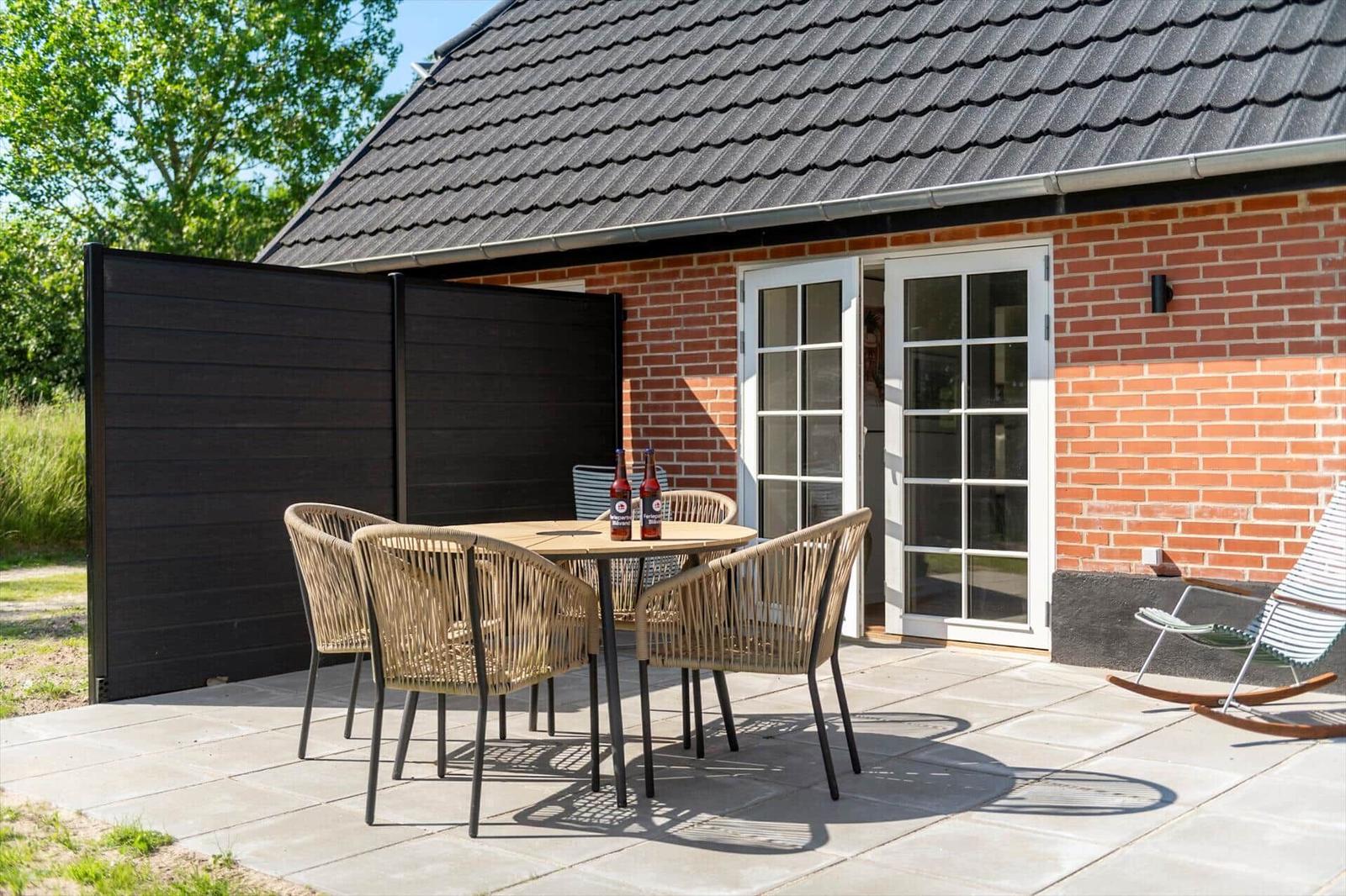 Terrasse mit Tisch, Stühlen und Schaukel vor einem Backsteinhaus mit Glastür.