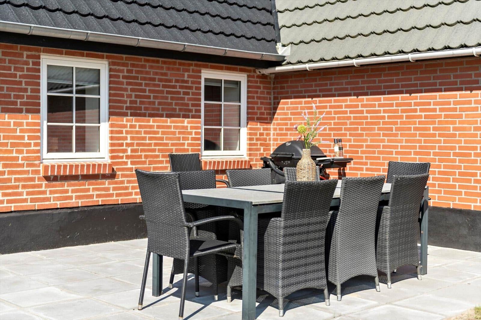Terrasse mit Tisch, Stühlen und Grill vor rotem Backsteinhaus.