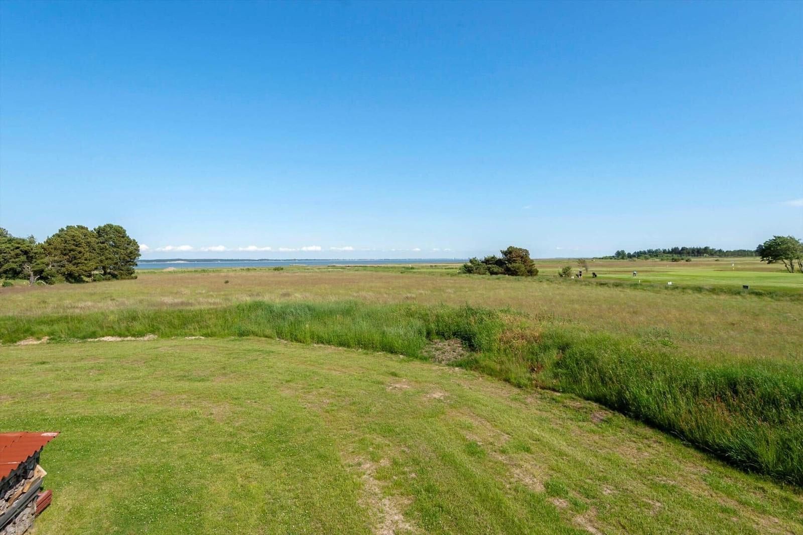 Weitläufiger Grasbereich mit Blick auf Golfplatz und Wasser unter blauem Himmel.