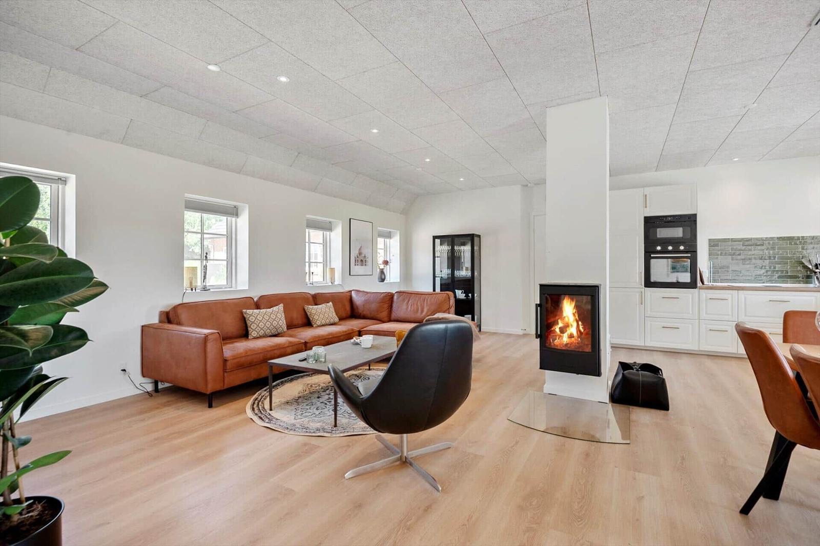 Wohnzimmer mit Sofa, Kamin und Küche im Hintergrund.