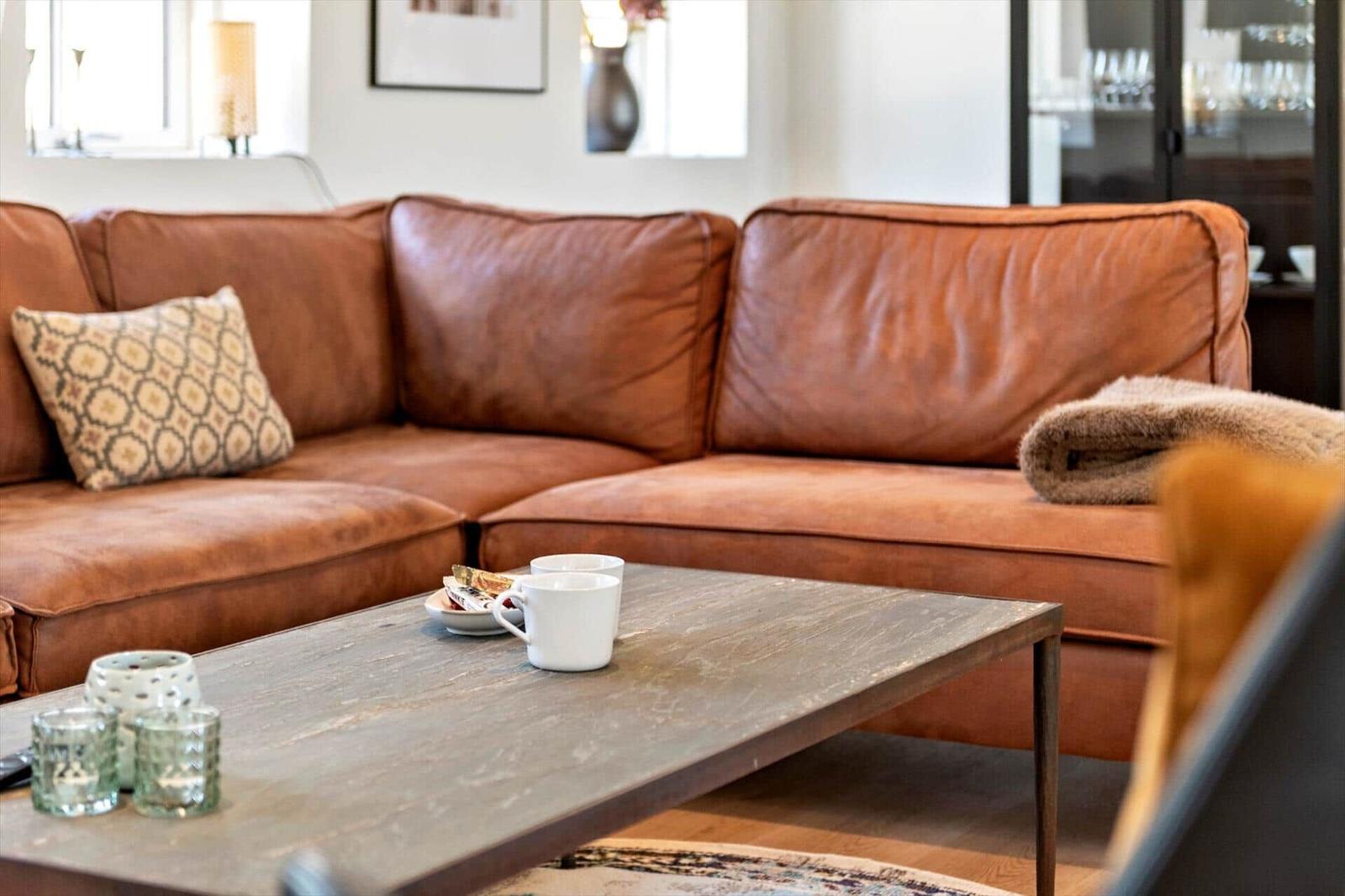 Ein braunes Ledersofa mit Kissen und Decke steht vor einem Holztisch mit Tassen.