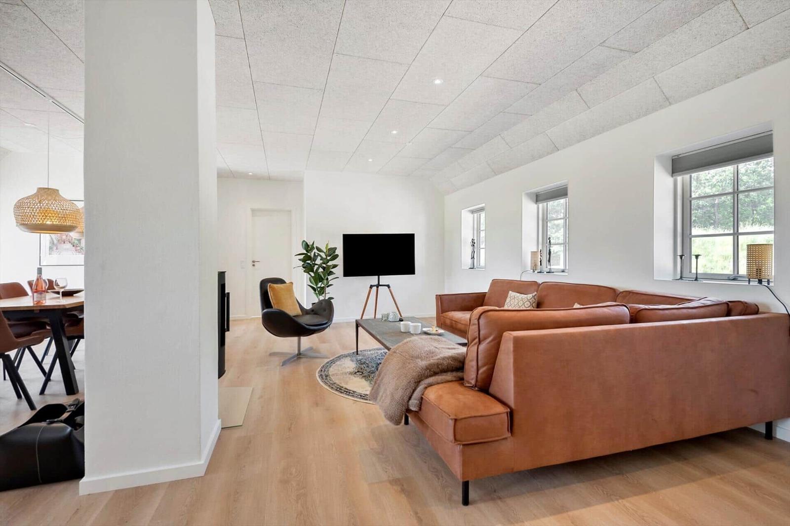 Wohnzimmer mit braunem Sofa, Fernseher und Holzboden. Blick in die Küche.