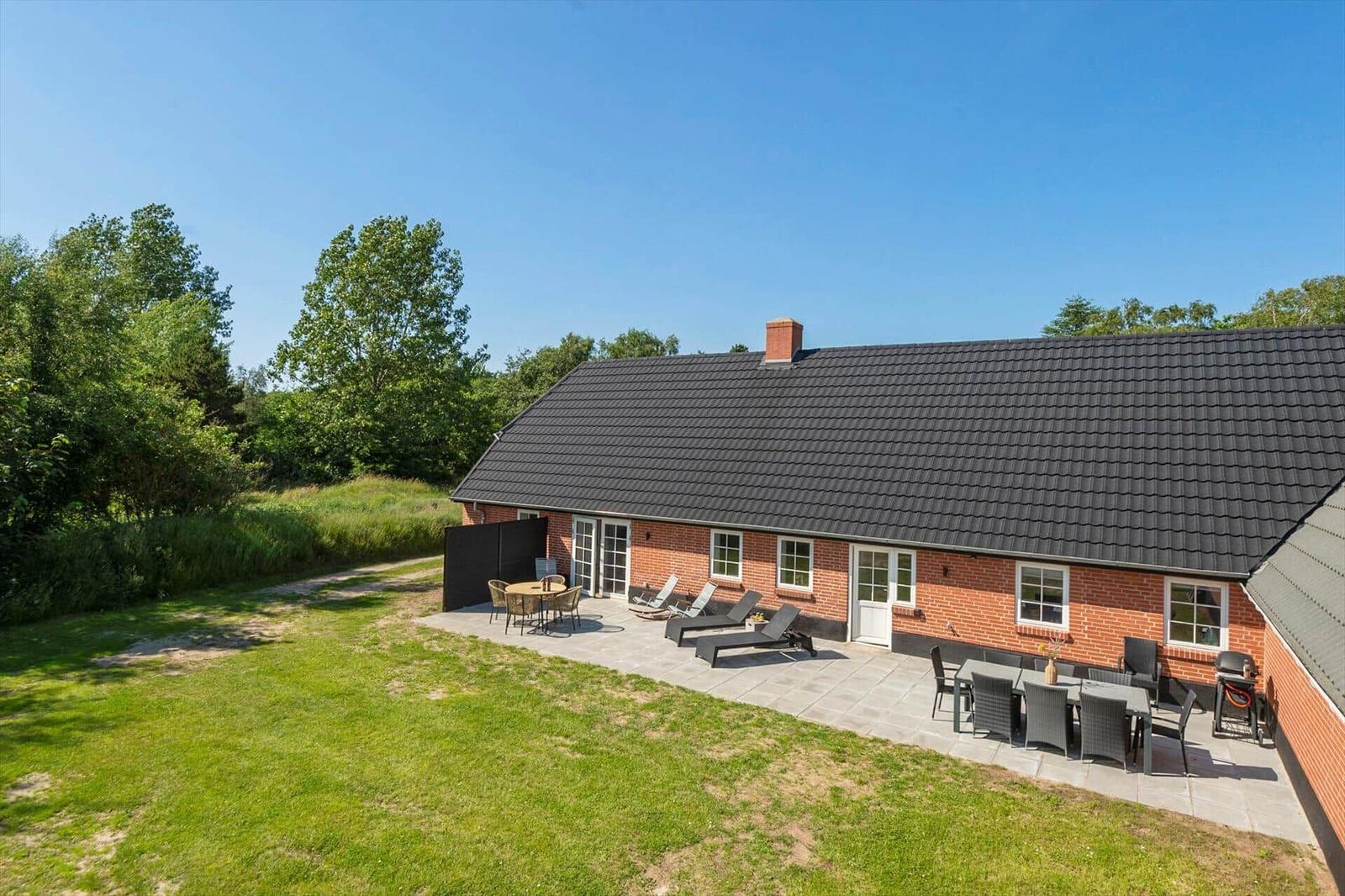 Ein Haus mit Terrasse, Liegestühlen und Grillplatz im Freien.