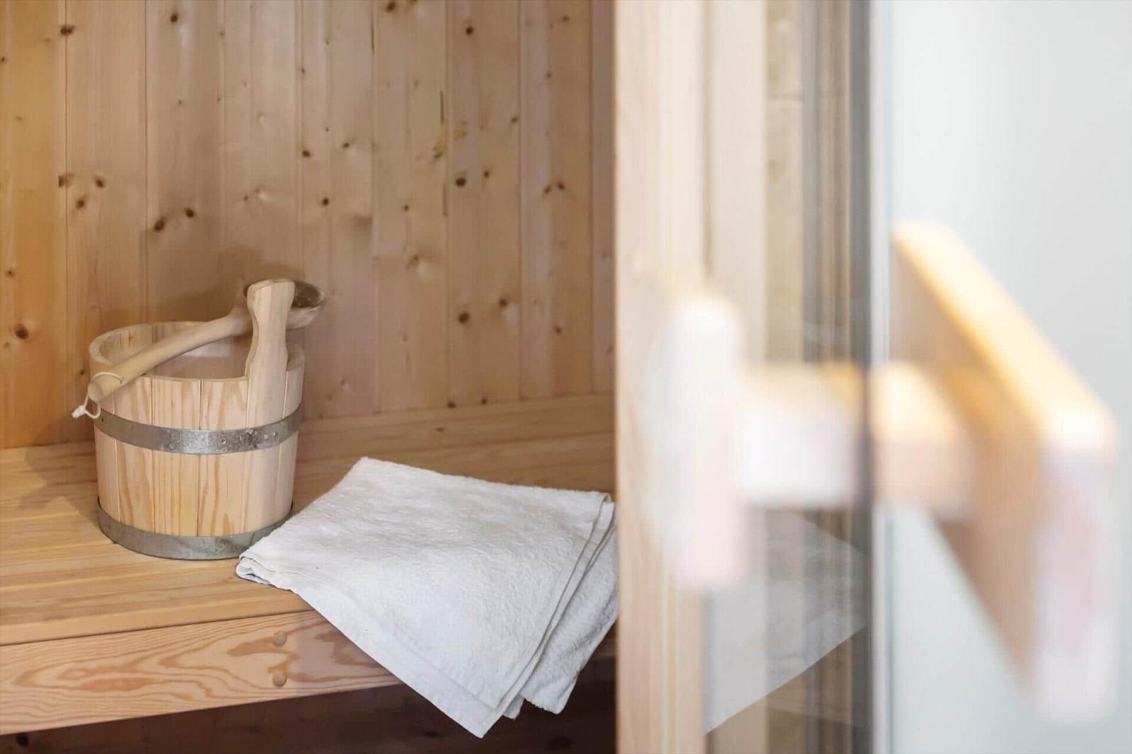 Sauna mit Holzbank, Holzkanister und weißem Handtuch.