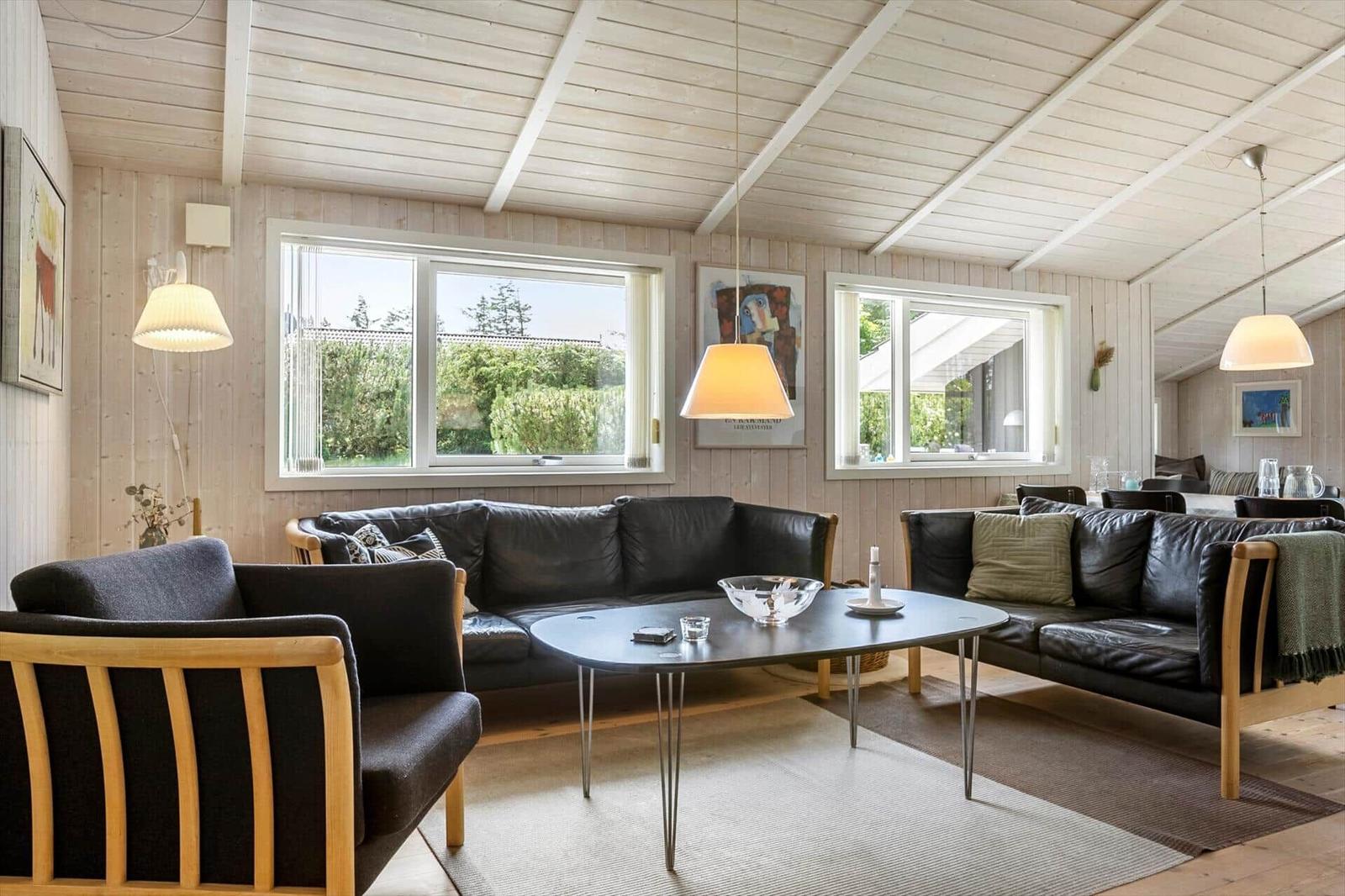 Wohnzimmer mit zwei schwarzen Sofas, einem ovalen Tisch und Holzwänden.