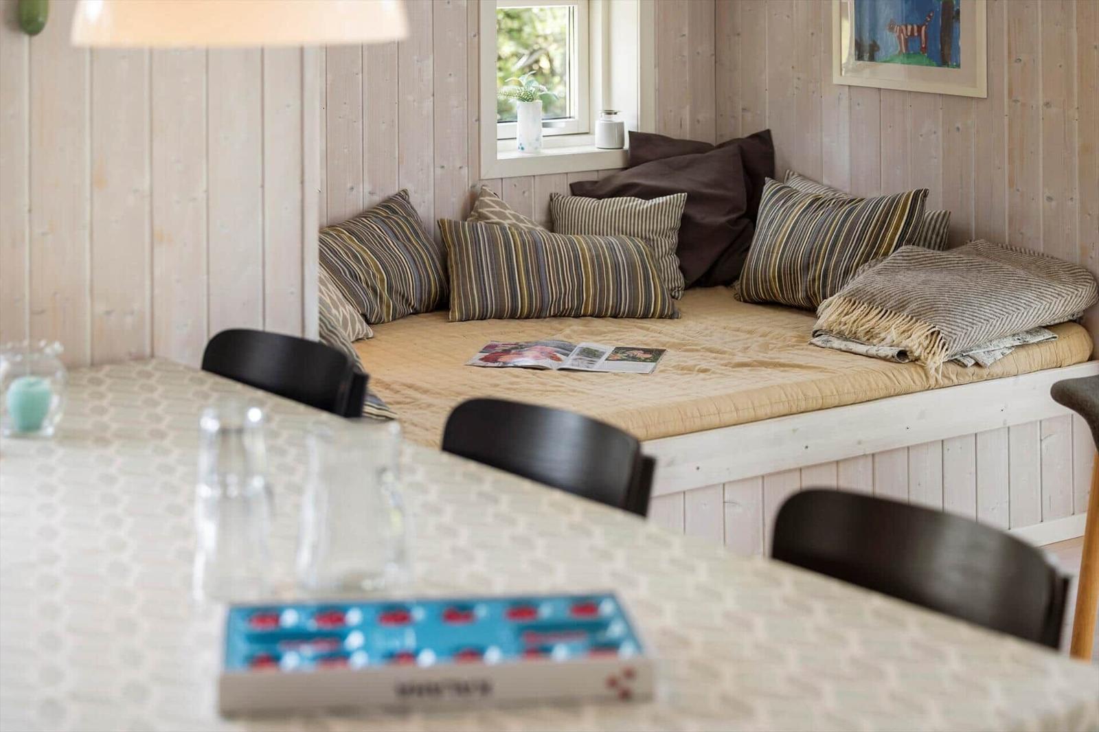Sitzbank mit Kissen und Decke an Wand, Tisch mit Stühlen im Vordergrund.