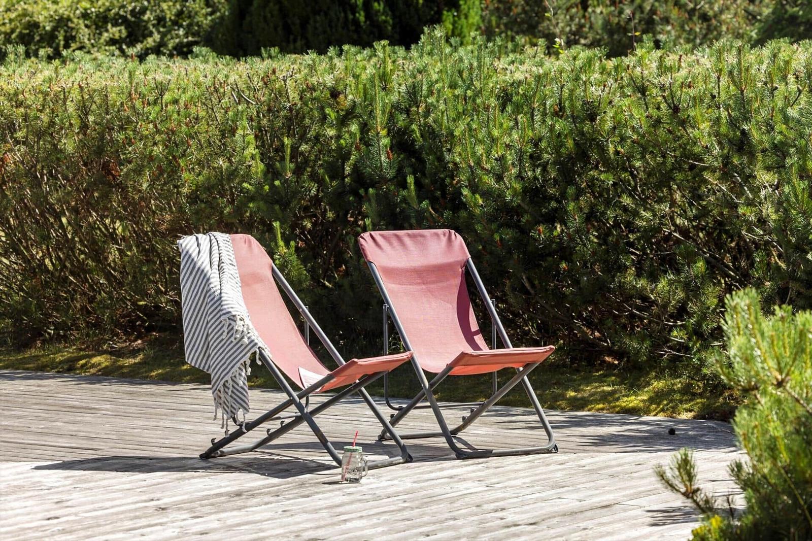 Zwei rosa Liegestühle auf einer Holterrasse mit grüner Hecke im Hintergrund.