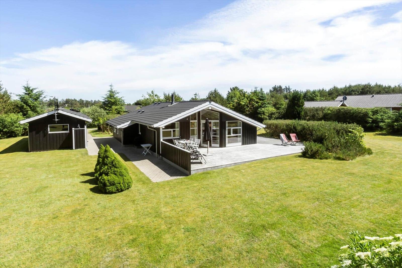 Holzhaus mit Terrasse, Garten und Liegestühlen. Nebenhaus und Wald im Hintergrund.