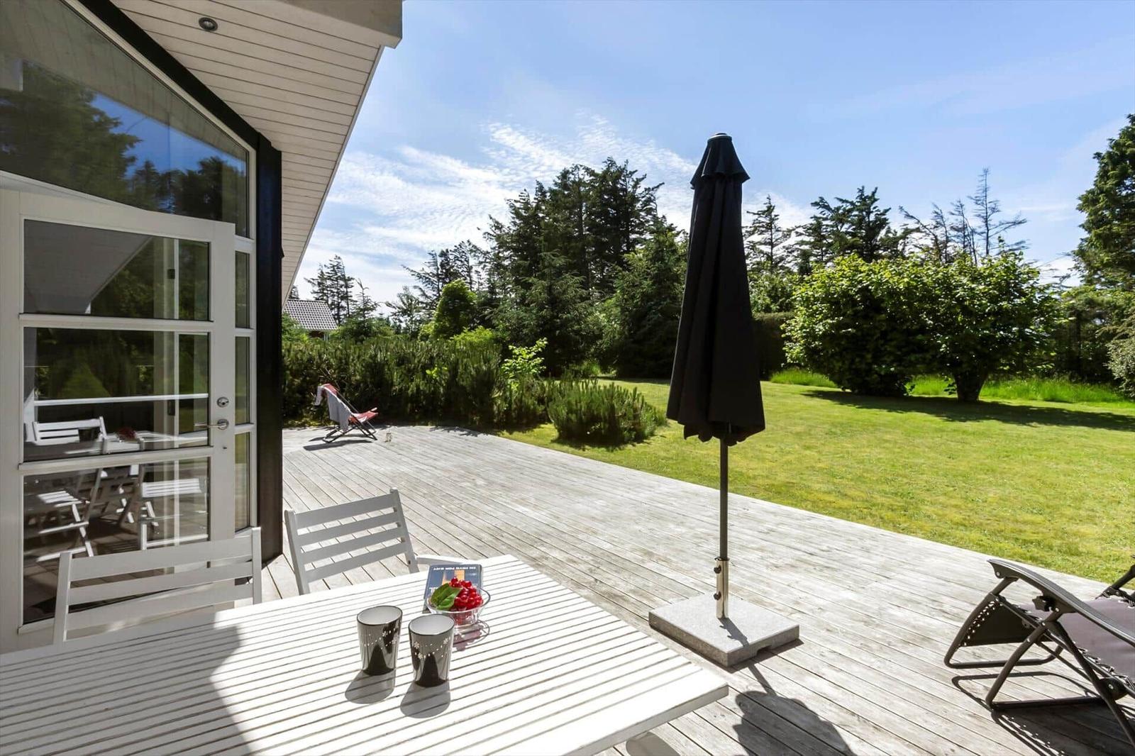 Terrasse mit Tisch, Stühlen und Sonnenschirm. Blick auf grünen Garten und Bäume.