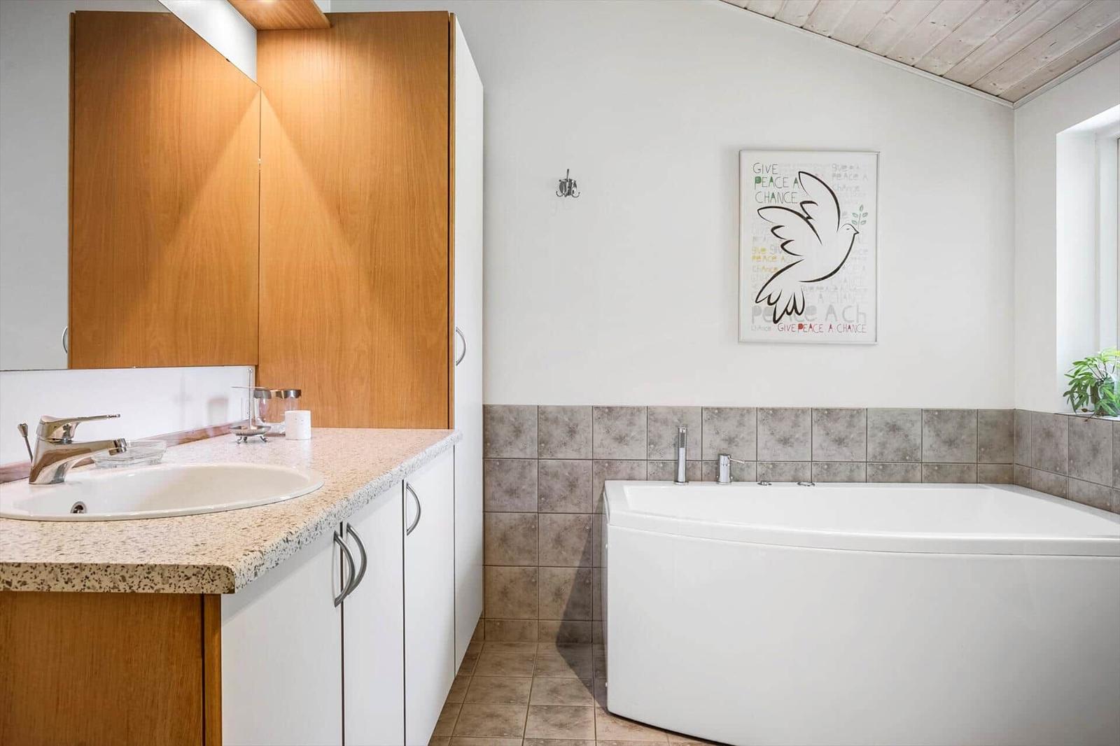 Badezimmer mit Badewanne, Waschbecken und Holzschränken. Wandbild mit Friedensmotiv.