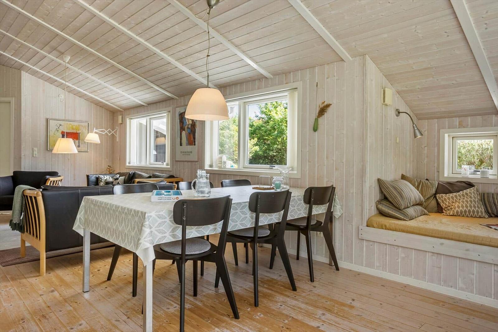 Esszimmer mit Tisch, Stühlen und Fenstern. Eckbank mit Kissen. Holzwände und Boden.