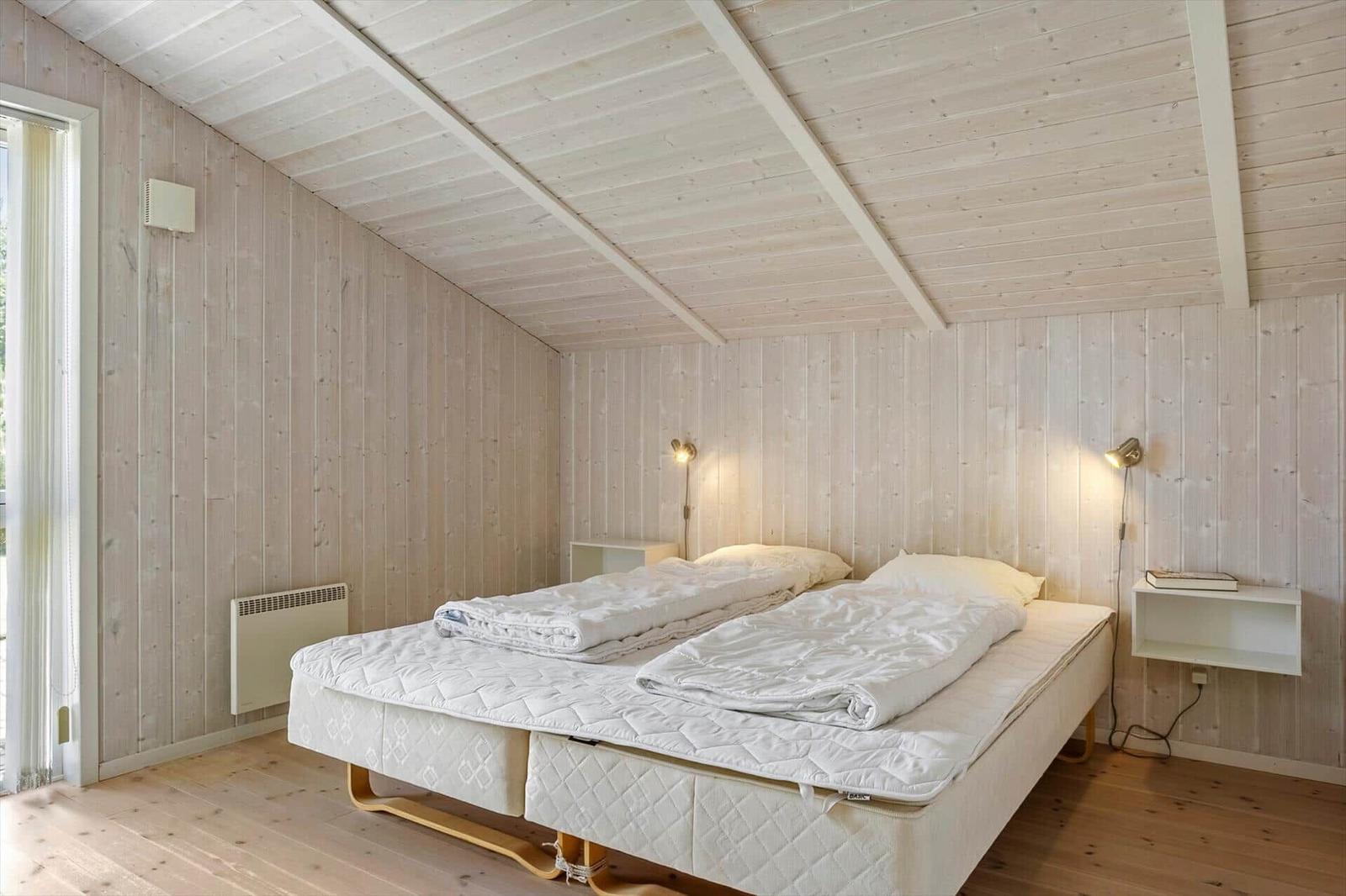 Schlafzimmer mit Holzwand, Doppelbett und Wandlampen.