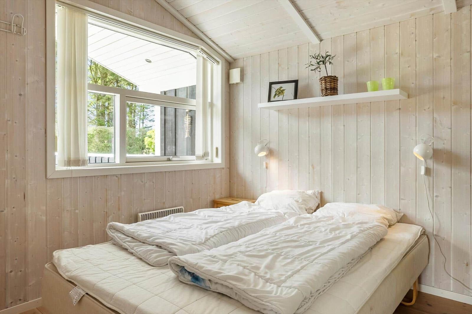 Schlafzimmer mit Holzwand, Fenster und Bett mit weißen Bettwäsche.