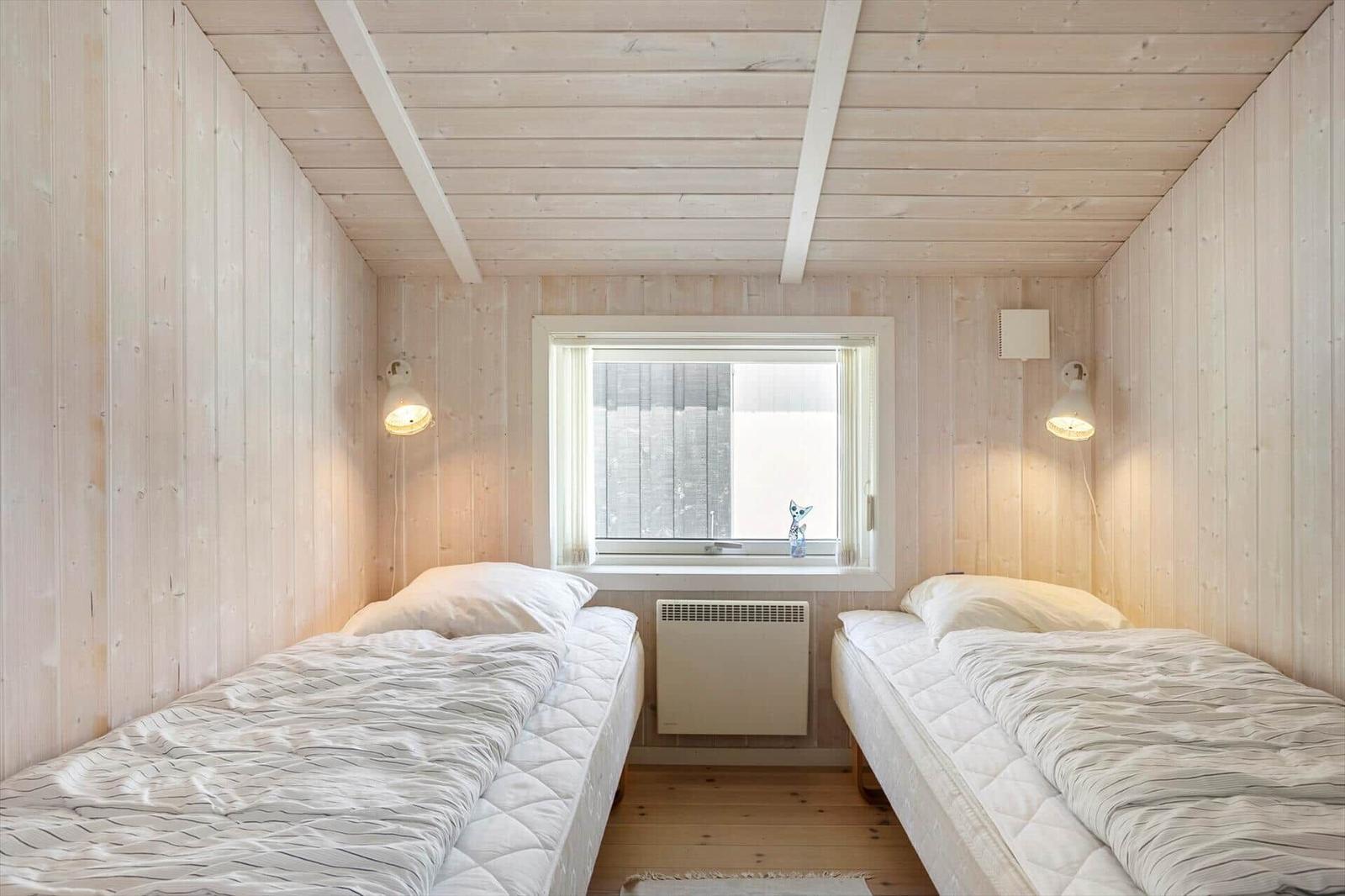 Zwei Betten in einem holzverkleideten Raum mit Fenster und Heizkörper.