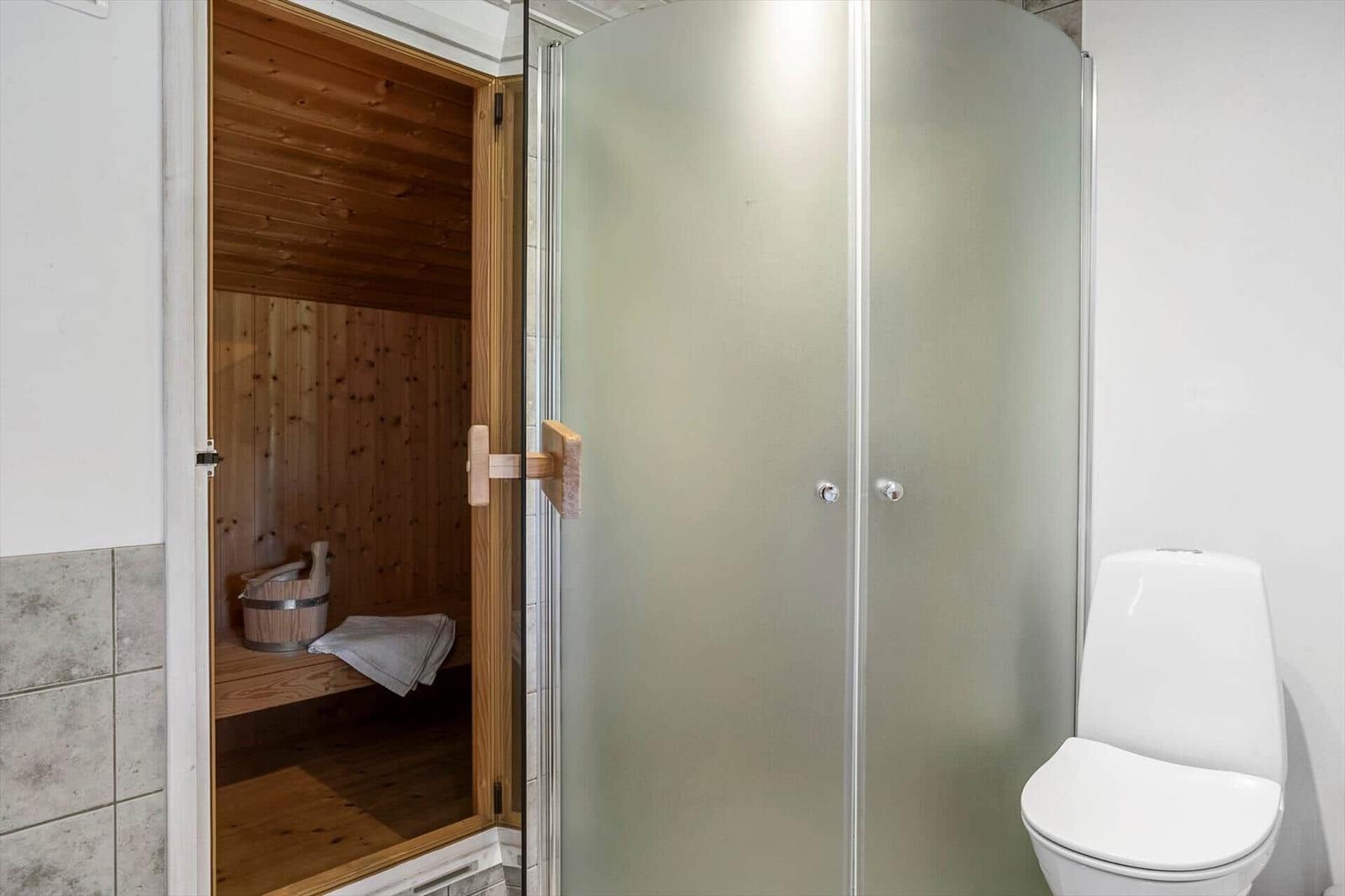 Dusche mit Duschwand, Toilette und integrierte Sauna mit Holzbank und Eimer.