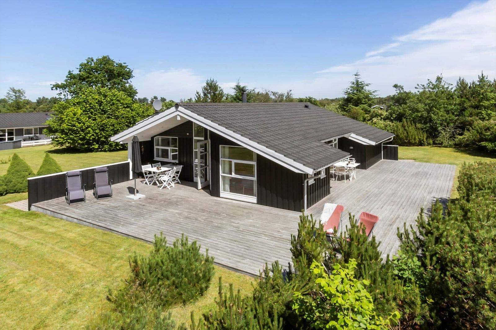Moderne Ferienhaus mit großem Holzdeck, Garten und Terrassenmöbeln.