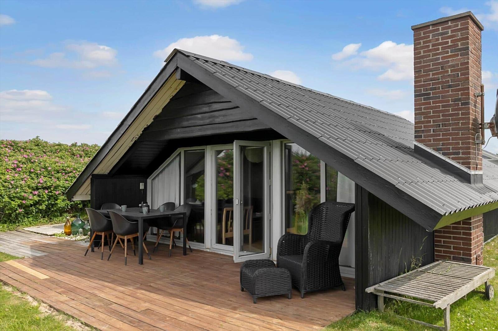 Haus mit Terrasse, Gartenmöbeln und Schornstein. Blick auf grüne Landschaft.