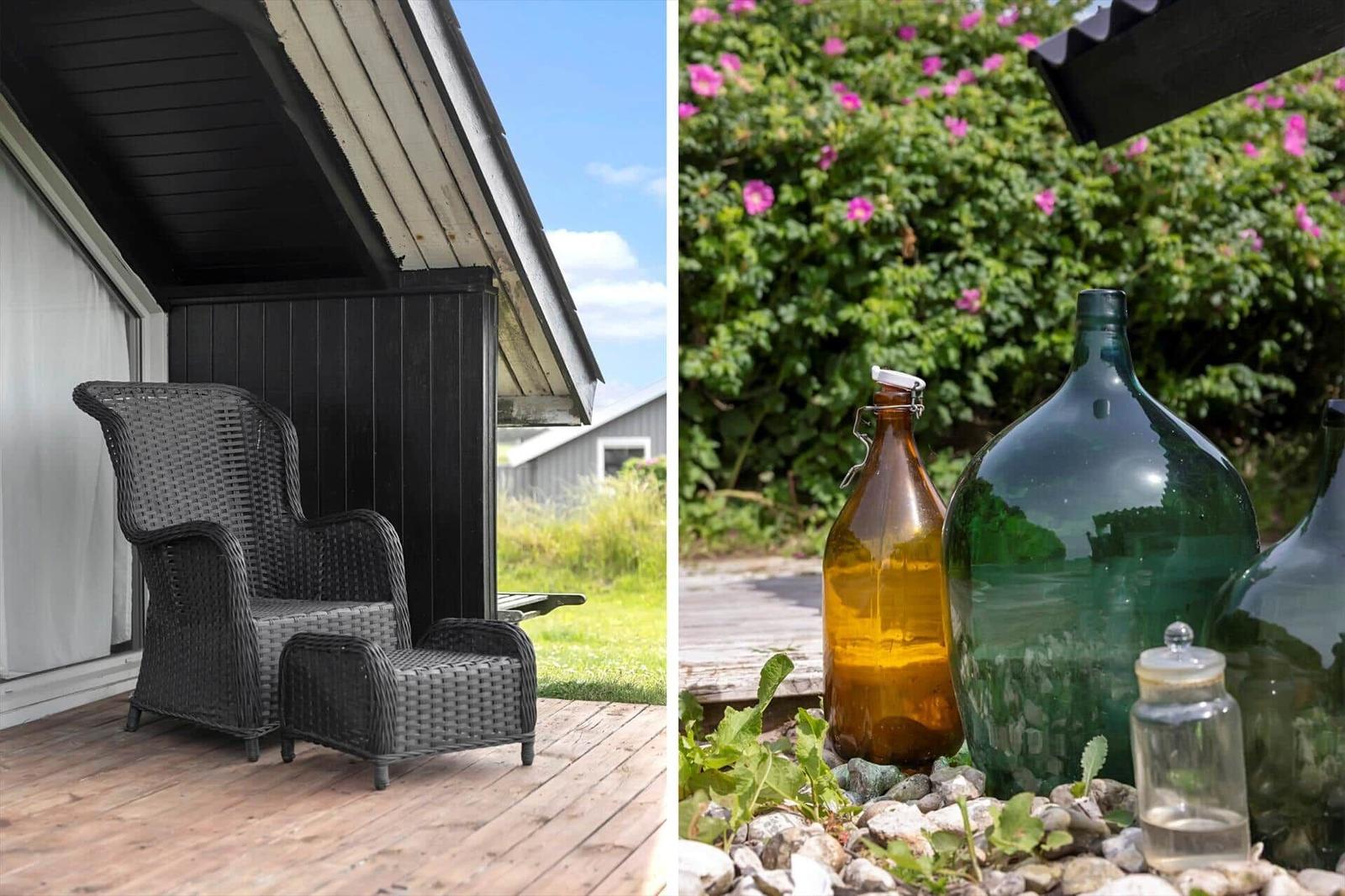 Schwarzer Wicker-Sessel auf Terrasse. Große Glasbehälter im Garten mit rosa Blumen.