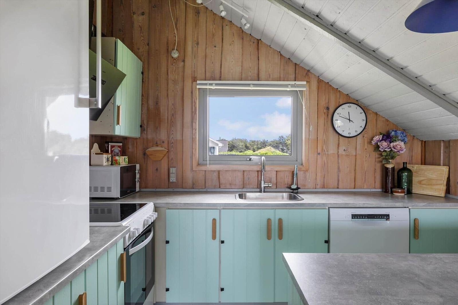 Küche mit Holzwand, Fenster, Spüle und hellblauen Schränken.