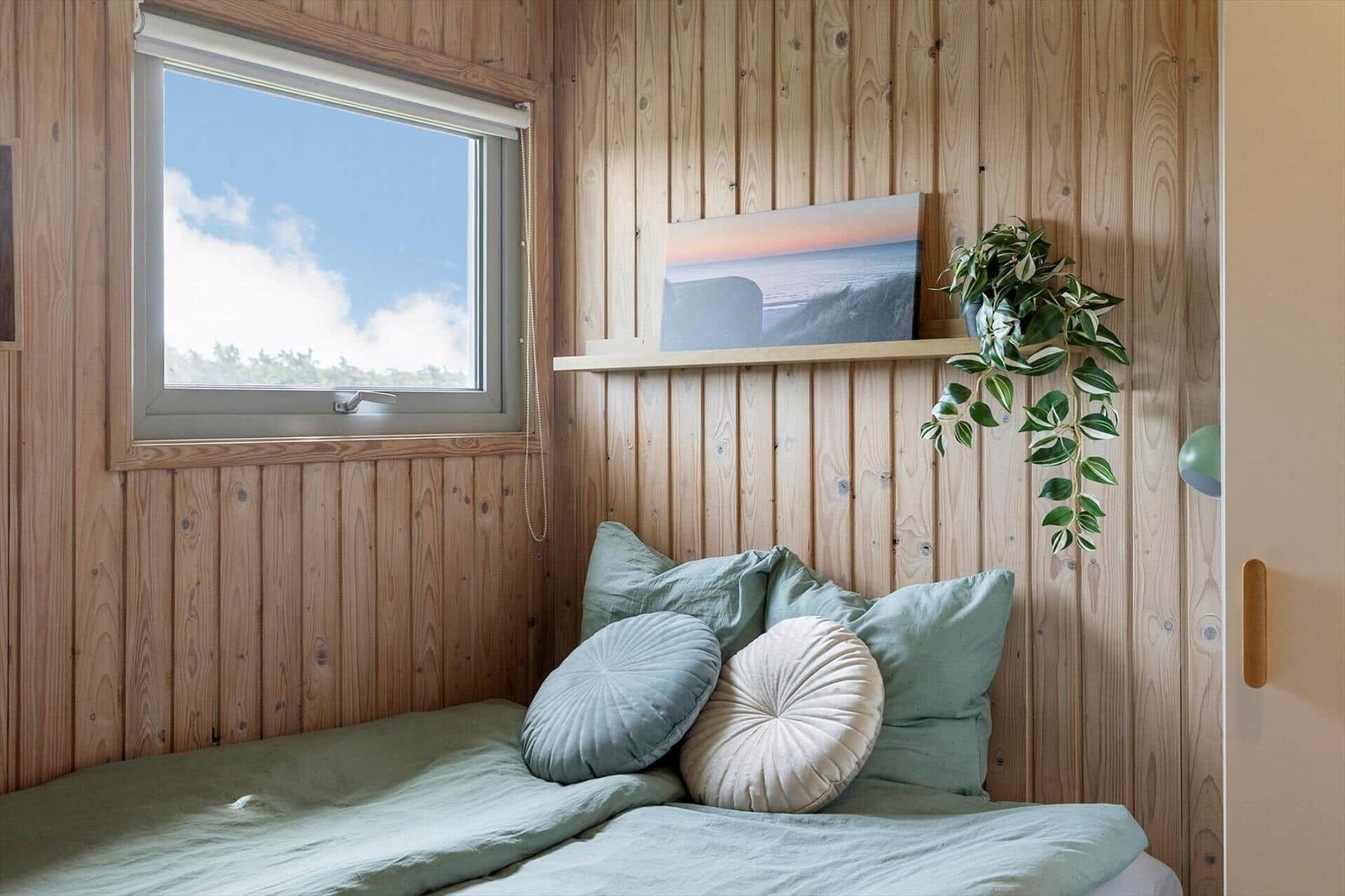 Schlafzimmer mit Holzwand, Bett, Kissen und Fenster mit Blick.