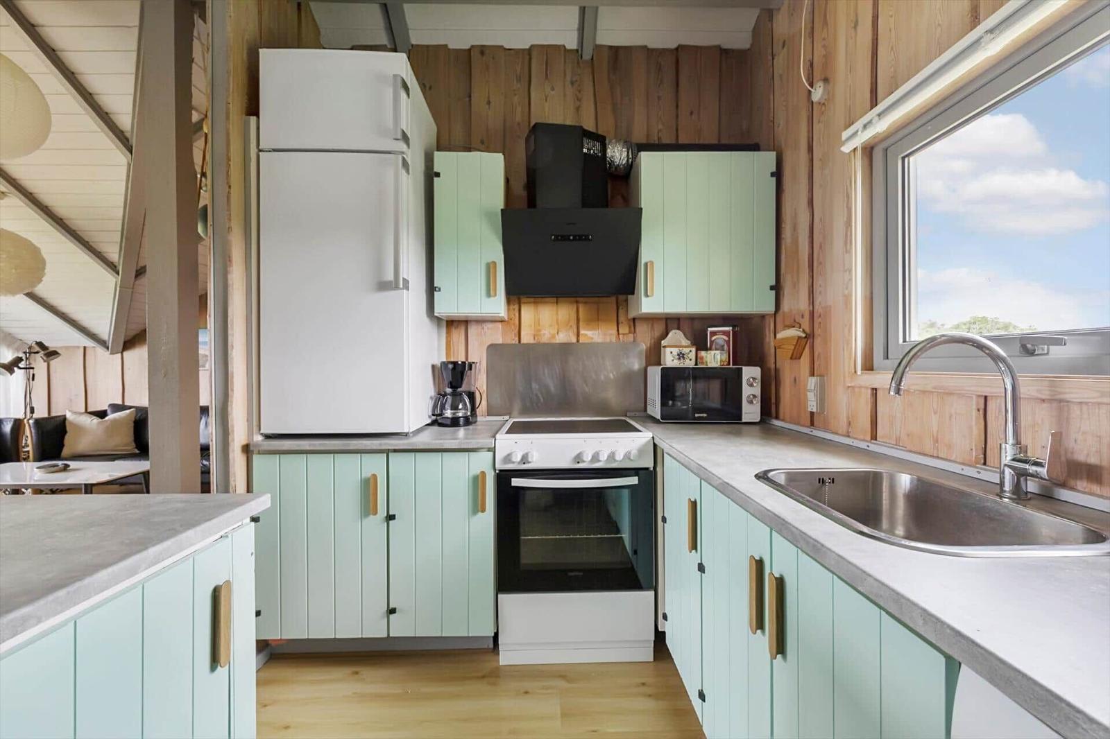 Küche mit Holzwänden, mintgrünen Schränken und moderner Arbeitsplatte.