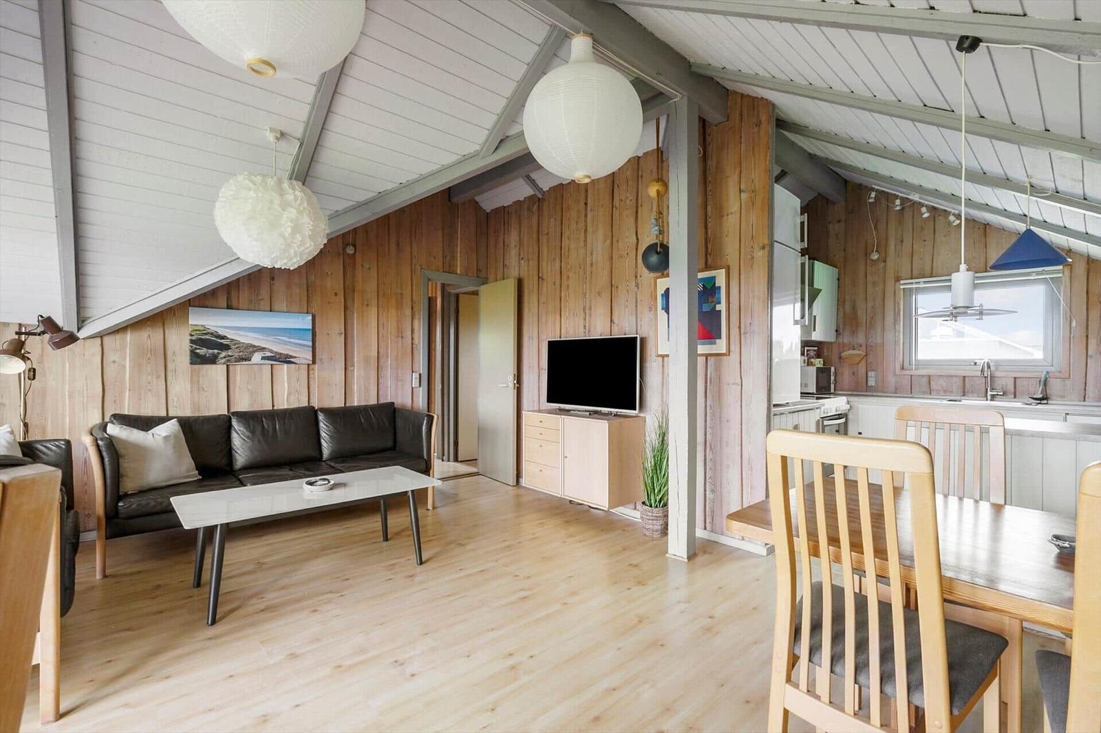 Wohn- und Essbereich mit Holzwand, Sofa, TV und Küchenbereich.