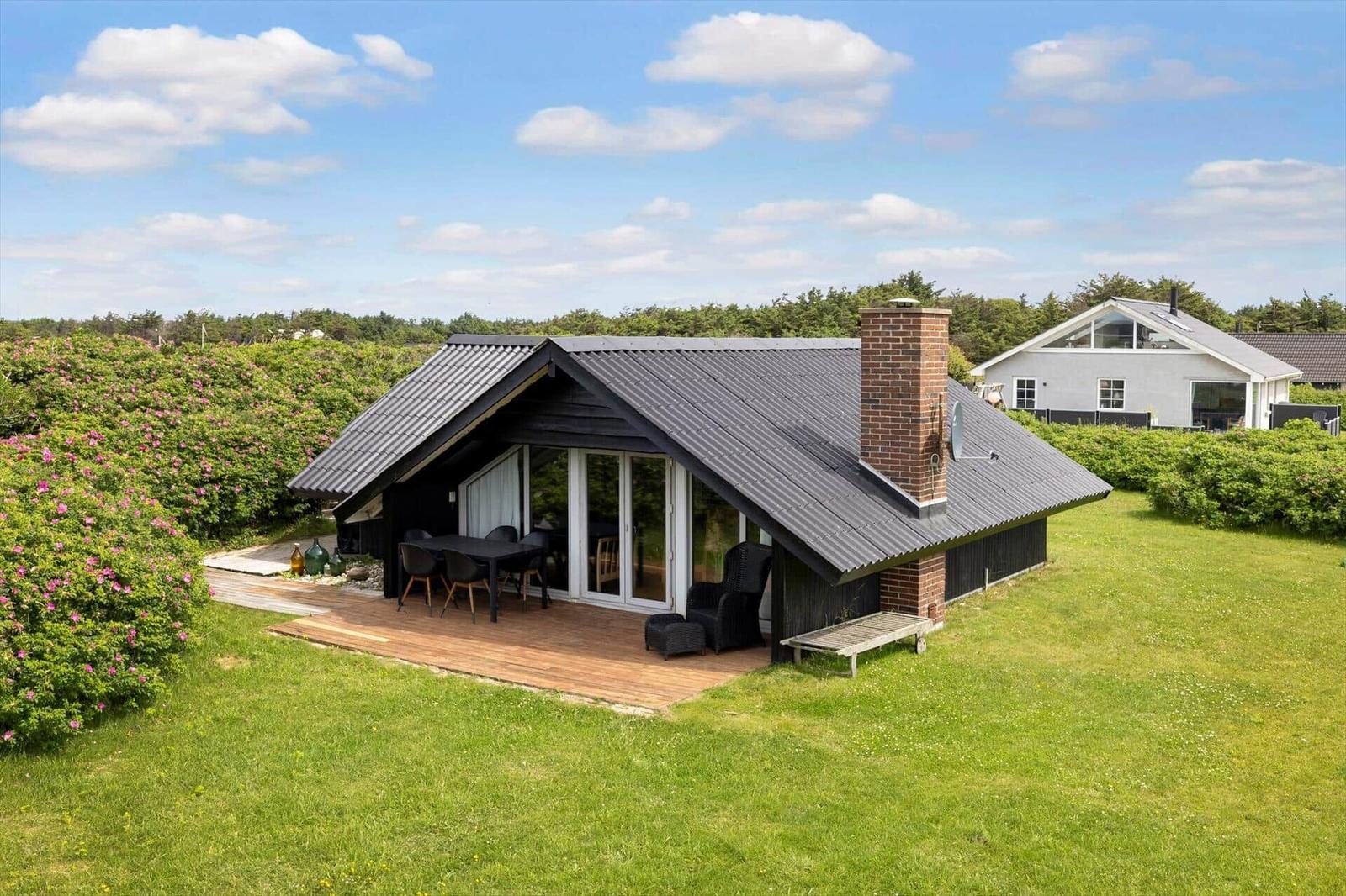 Moderne Villa mit Holzterrasse, Garten und Grillplatz unter blauem Himmel.