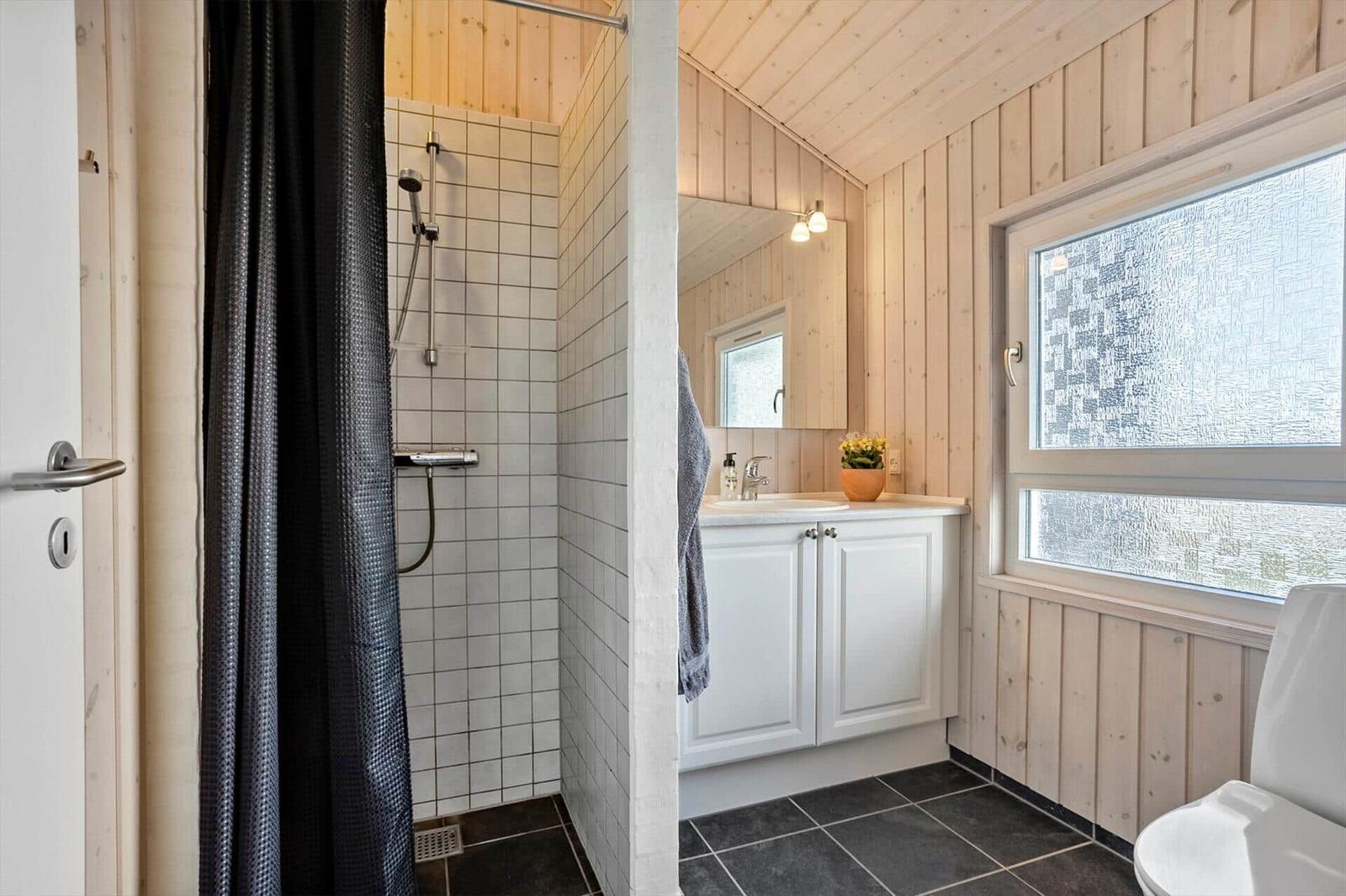 Badezimmer mit Dusche, Waschbecken und Toilette. Holzwände und Fenster mit Muster.