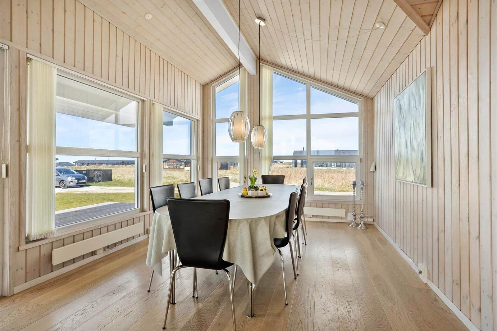 Esszimmer mit Tisch, Stühlen und großen Fenstern. Holzwände und Boden.