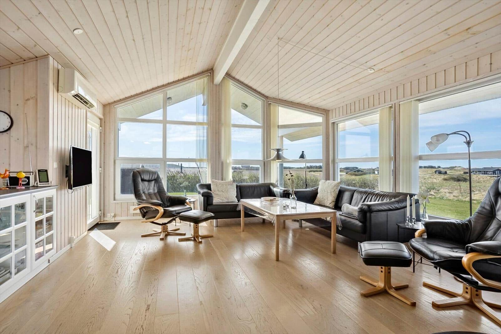 Wohnzimmer mit Holzboden, großen Fenstern und schwarzer Ledermöbelgruppe.