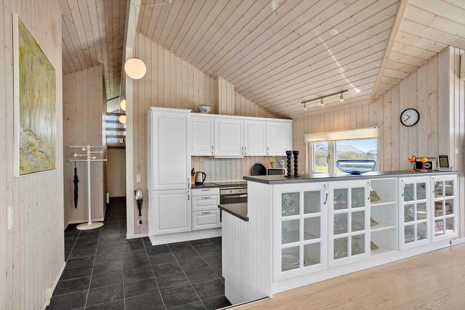 Küche mit weißer Einbauküche, Glasfrontschrank und Holzwandverkleidung.