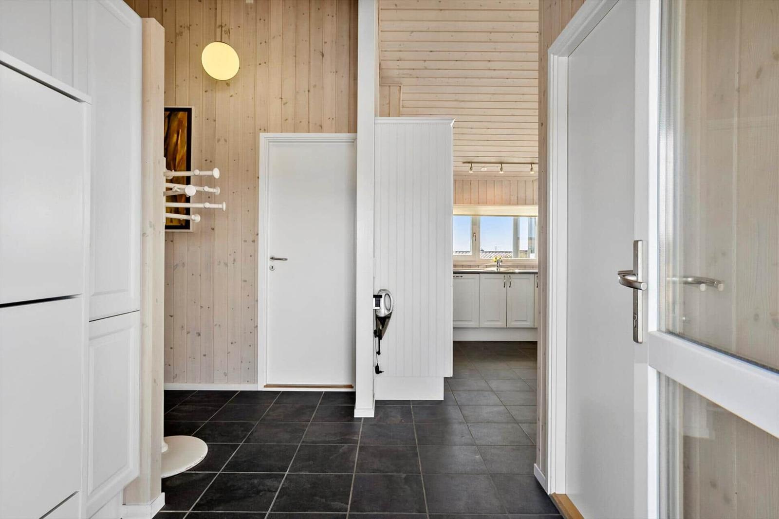 Hallenraum mit Holzwand, weißen Türen und dunklem Boden. Küche im Hintergrund sichtbar.