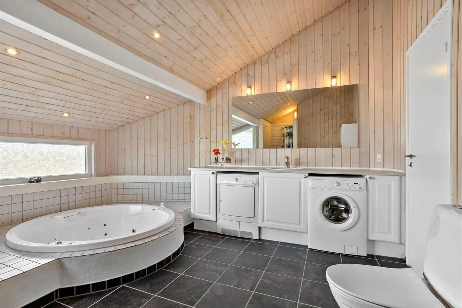 Badezimmer mit Whirlpool, Waschmaschine und Trockner. Holzwand und dunkler Boden.