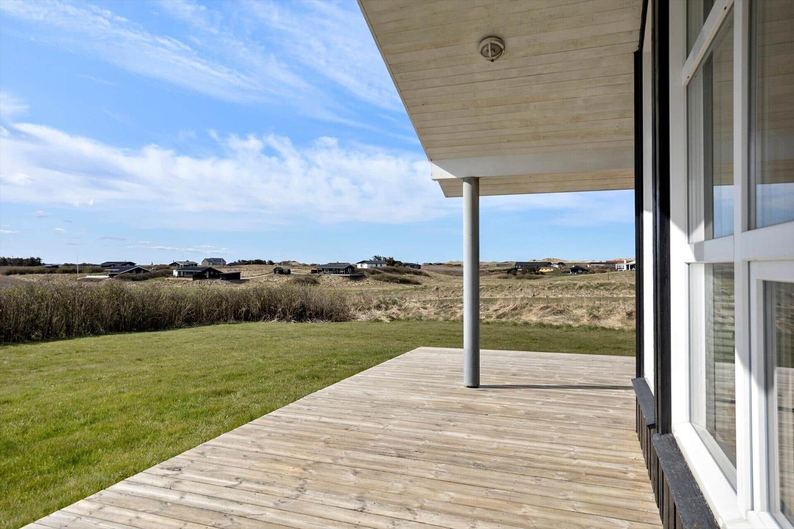 Terrasse mit Holzdecke und Blick auf Grasland und Ferienhäuser.