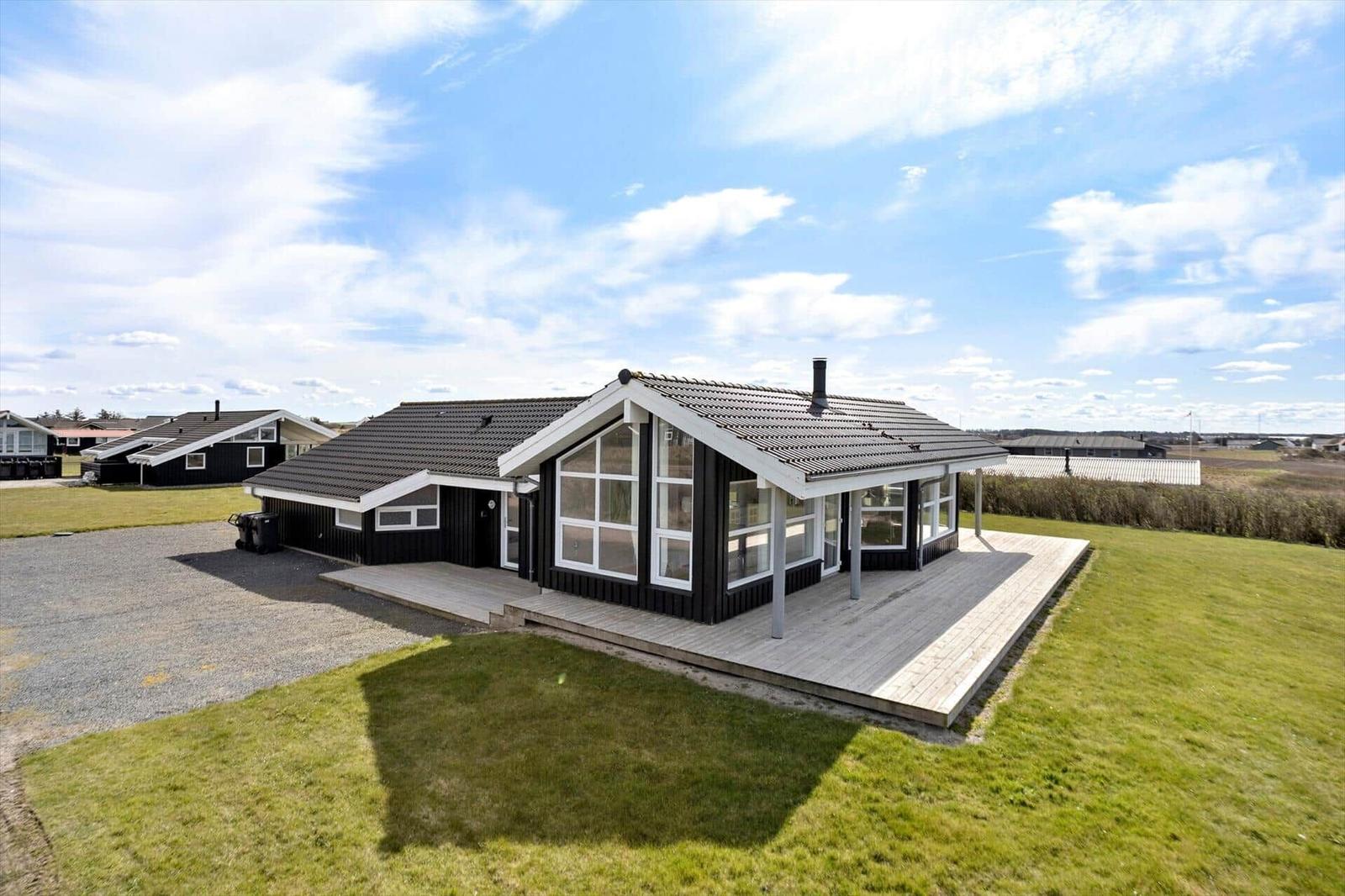 Moderne Villa mit Holzveranda und großzügigem Grundstück unter blauem Himmel.