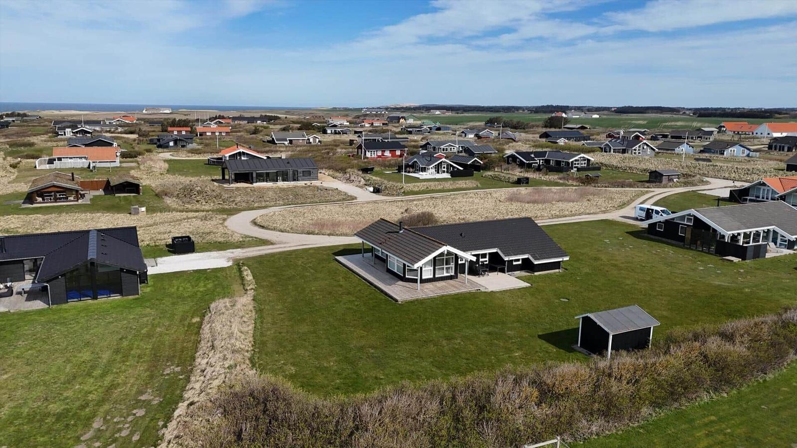 Haus mit Terrasse und Garten, umgeben von Grasland und weiteren Häusern in der Ferne.