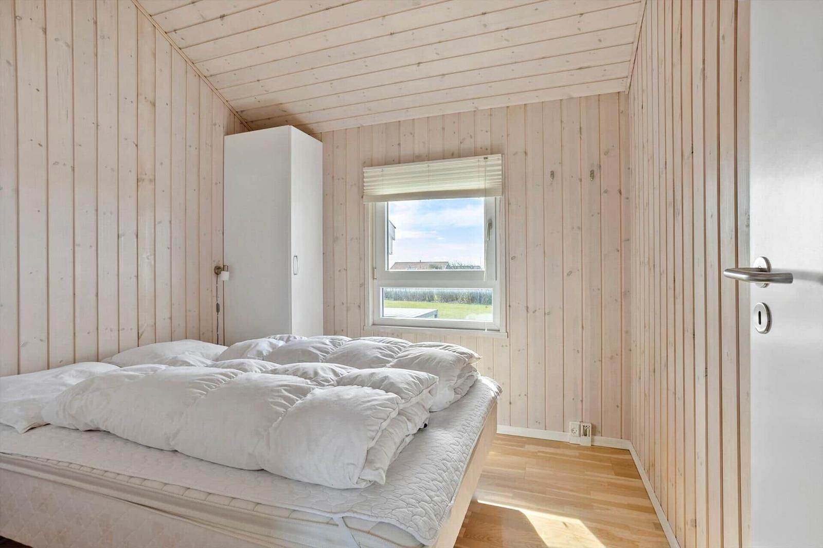 Schlafzimmer mit Holzwand, Bett, Fenster und Schrank.