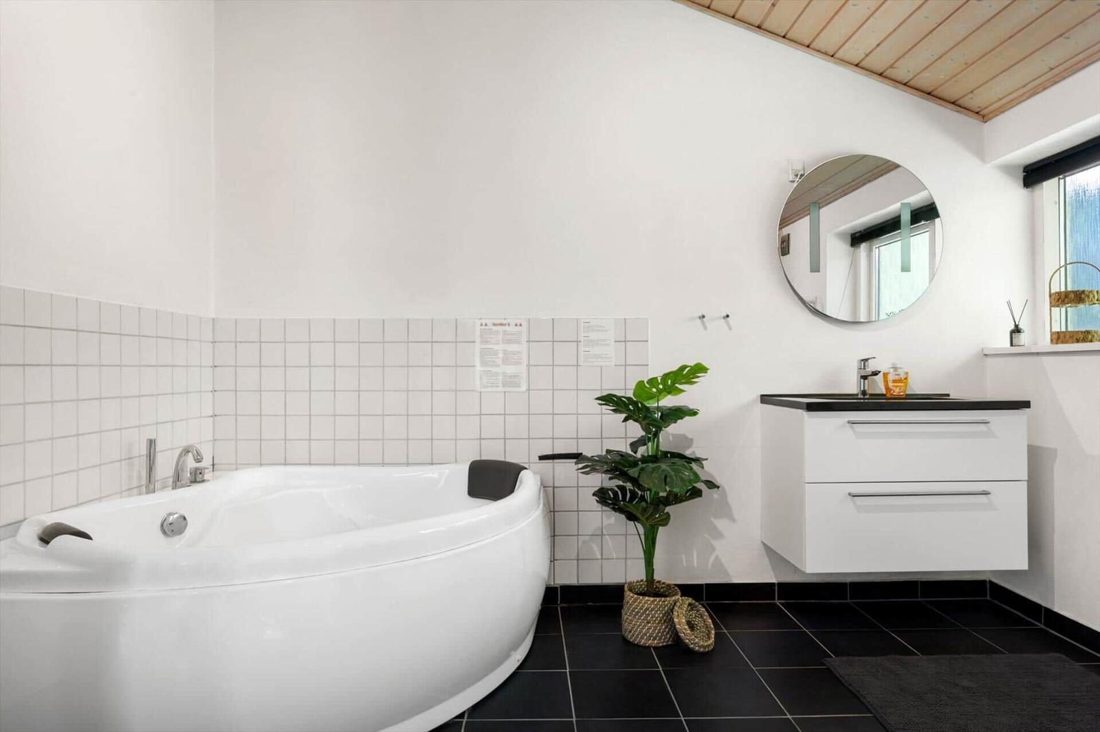 Badezimmer mit Badewanne, Waschbecken und Pflanze.