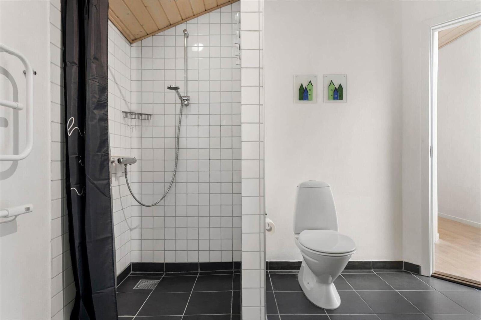 Bad mit Dusche, Toilette und schwarzem Bodenfliesen.