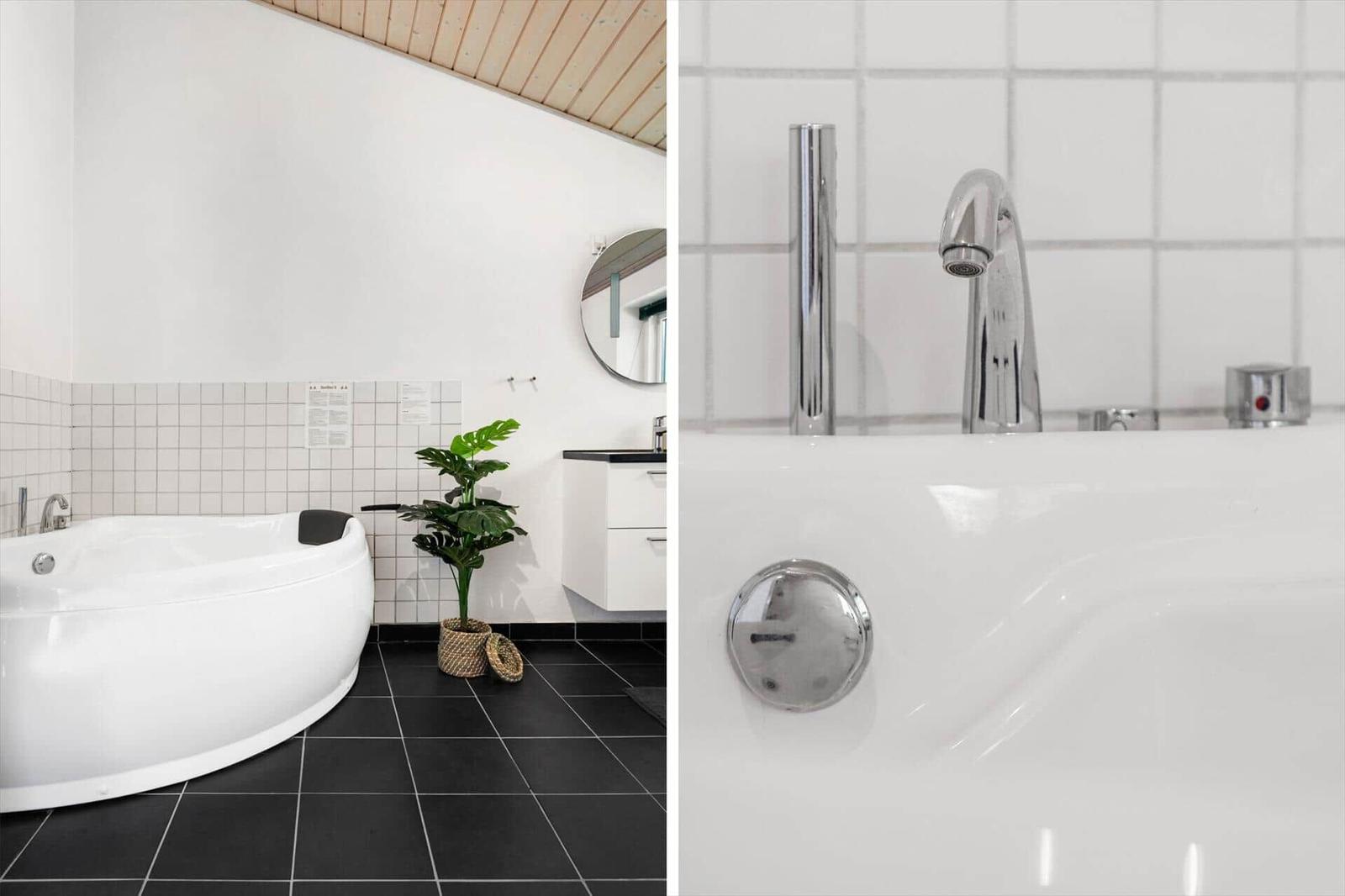 Badezimmer mit weißer Badewanne, schwarzen Fliesen und Pflanze.