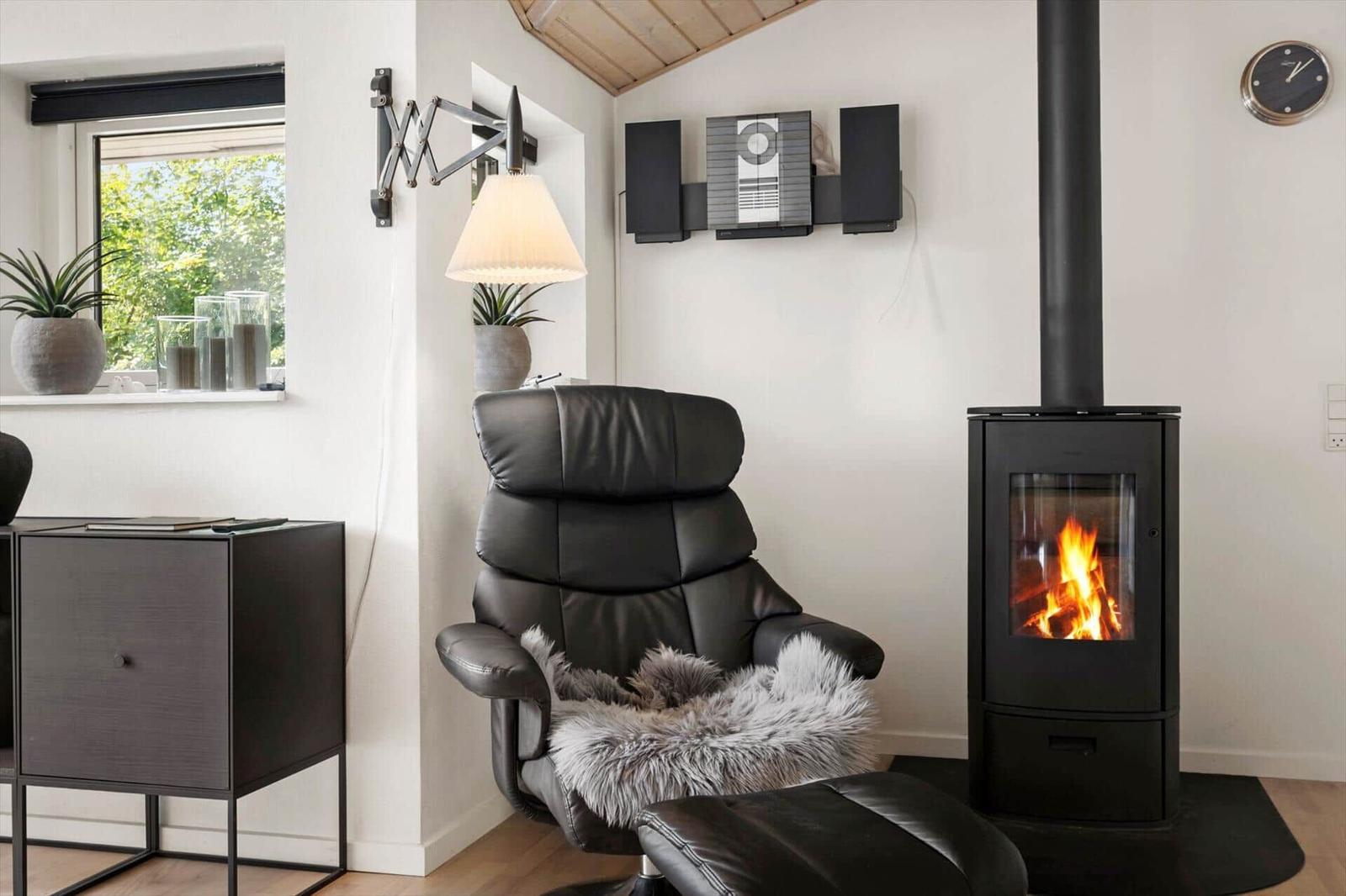 Ein schwarzes Ledersessel mit Felldecke steht vor einem Kamin mit brennendem Feuer.