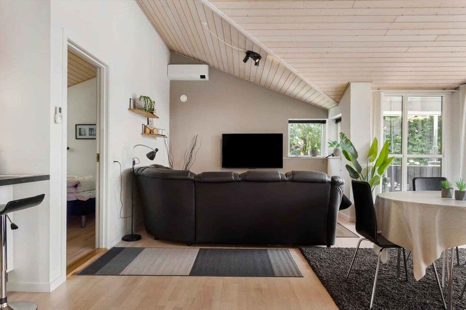 Wohnbereich mit Sofa, TV und Essbereich unter Holzdecke.