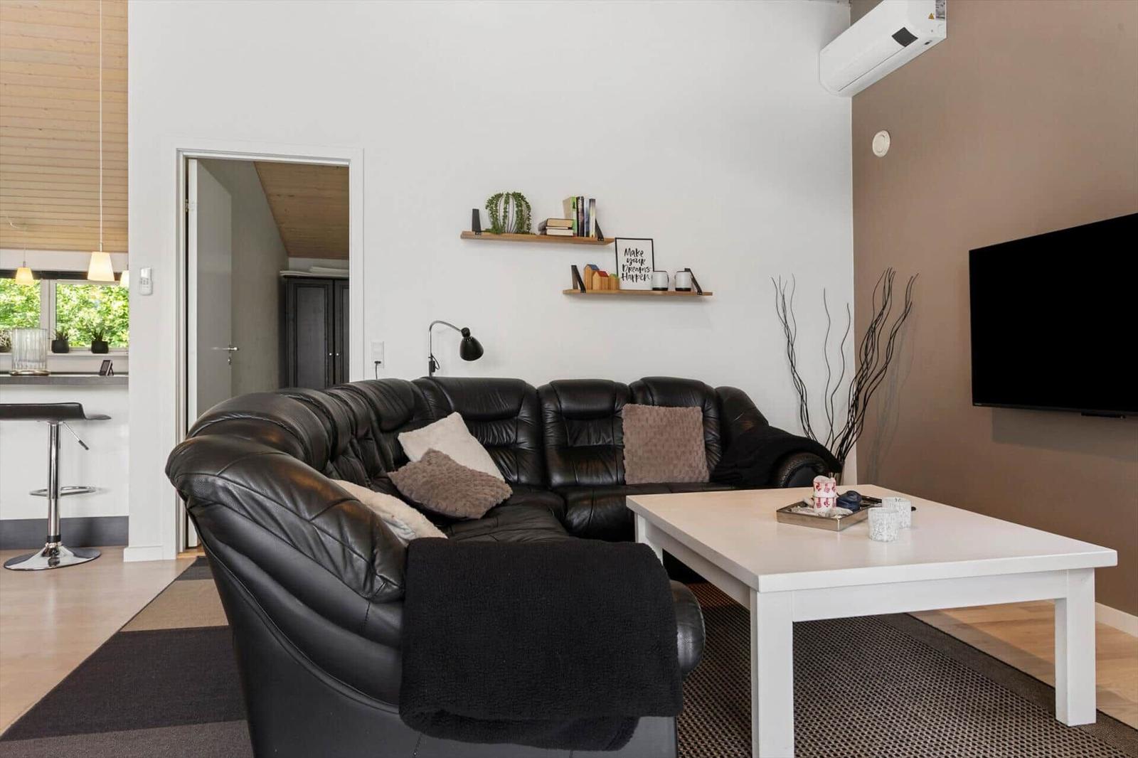 Schwarzes Ledersofa, weißer Couchtisch, Wandregale mit Deko, Flachbild-TV an der Wand.