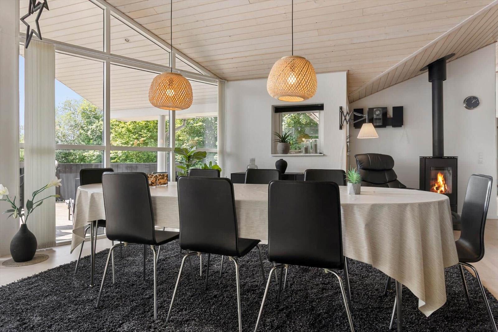 Esszimmer mit runder Tisch, schwarzen Stühlen und Kamin. Große Fenster bieten Blick auf Garten.